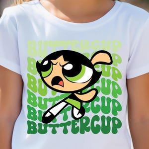 May include: White t-shirt with a green cartoon character of Buttercup from the Powerpuff Girls. The character is kicking and has an angry expression. The background is filled with the word "Buttercup" repeated in a green gradient.