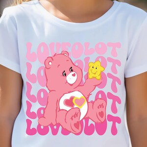 May include: White t-shirt with a pink Care Bear holding a yellow star. The shirt has the word "LOVE" repeated in pink letters.