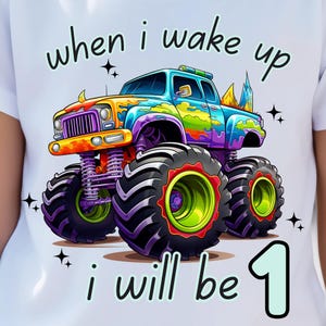 May include: White t-shirt featuring a colorful monster truck graphic. The truck is decorated with vibrant hues of blue, purple, yellow, and green. Text on the shirt reads "when i wake up i will be 1". Black star accents surround the text and truck.
