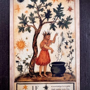Peut inclure: Carte de tarot illustrée avec une femme couronnée en robe orange, près d'un arbre et d'un chaudron fumant. La carte porte le mot "IF" et le texte "La connaissance est une porte qui s'ouvre dans le brouillard."