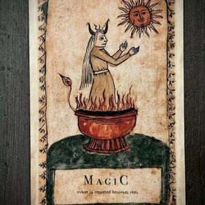 Può includere: Una carta rettangolare con un'illustrazione disegnata a mano di una figura cornuta con capelli lunghi in piedi in una ciotola rossa di fiamme, che tende le mani verso un sole. Il testo recita MAGIC e What is repeated becomes real.