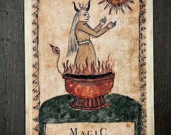May include: A rectangular card featuring a hand-drawn illustration of a horned figure with long hair standing in a red bowl of flames, reaching toward a sun. The text reads MAGIC and What is repeated becomes real. The border has a floral pattern.