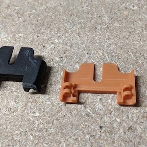 Può includere: Due pezzi di plastica stampati in 3D, uno nero e uno arancione, con una fessura al centro. I pezzi sono progettati per essere assemblati.