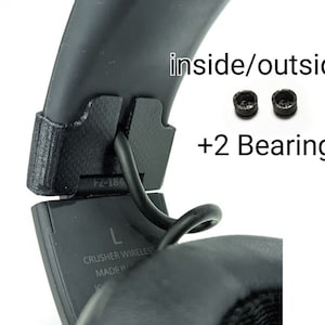 Op de afbeelding: Een close-up van een zwarte hoofdtelefoonband met een zwarte kabel eraan bevestigd. De band heeft een label met de tekst "Crusher Wireless" en "Made in China". De afbeelding toont ook twee kleine zwarte lagers.