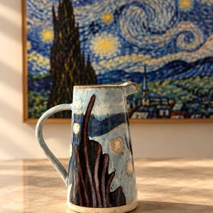 May include: A ceramic pitcher featuring a hand-painted design of a dark, tall cypress tree against a light blue, swirling night sky with yellow circular stars. The pitcher has a curved handle, a small pouring spout, and a speckled finish.