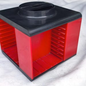 以下が含まれることがあります： 赤と黒のプラスチック製フィルムキャニスター。立方体型のキャニスターは、黒い上部と赤い側面を持っています。上部には円形の開口部があります。側面には垂直のスロットがあります。フィルムを収納するように設計されています。