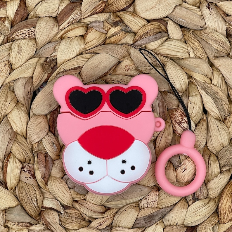 May include: Pink silicone phone case with a cartoon pink panther design. The case has a black heart-shaped sunglasses and a red nose. The case comes with a pink lanyard.