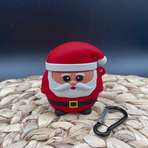 May include: Red and white Santa Claus character silicone case for Airpods with a black carabiner clip.