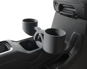 May include: Black plastic cup holder accessory for a car. The cup holder is attached to the center console and has two cup holders.