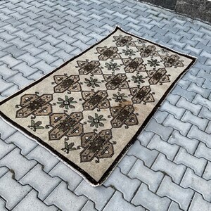 Puede incluir: Una alfombra beige con un patrón geométrico en marrón y verde. La alfombra tiene un diseño tradicional con detalles intrincados.