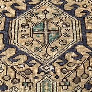 Peut inclure: Gros plan sur un tapis beige et bleu marine &agrave; motifs. Le tapis pr&eacute;sente une forme de losange central avec un motif de croix au centre, entour&eacute; de motifs floraux et g&eacute;om&eacute;triques complexes. Le tapis a un style vintage et traditionnel.