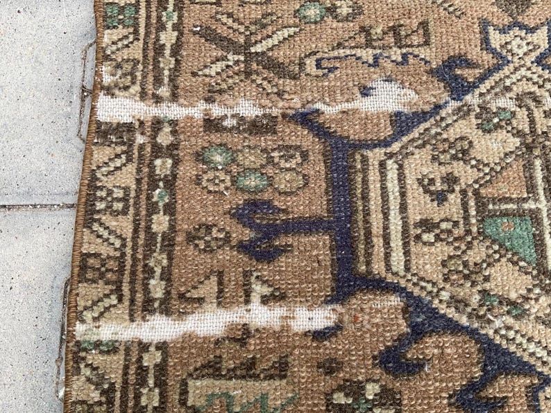 Peut inclure: Gros plan sur une section d'un tapis vintage &agrave; l'aspect vieilli. Le tapis pr&eacute;sente une palette de couleurs marron et beige avec des motifs g&eacute;om&eacute;triques complexes et une bordure bleu fonc&eacute;. Le design comprend des motifs floraux et stylis&eacute;s.