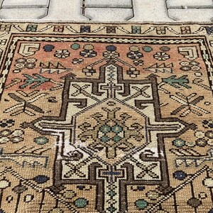 Peut inclure: Un tapis rectangulaire vintage avec un motif g&eacute;om&eacute;trique d&eacute;taill&eacute;. Le tapis pr&eacute;sente un motif de m&eacute;daillon central dans des tons de marron, beige et p&ecirc;che, avec des touches de bleu et de vert. La bordure est marron fonc&eacute;.