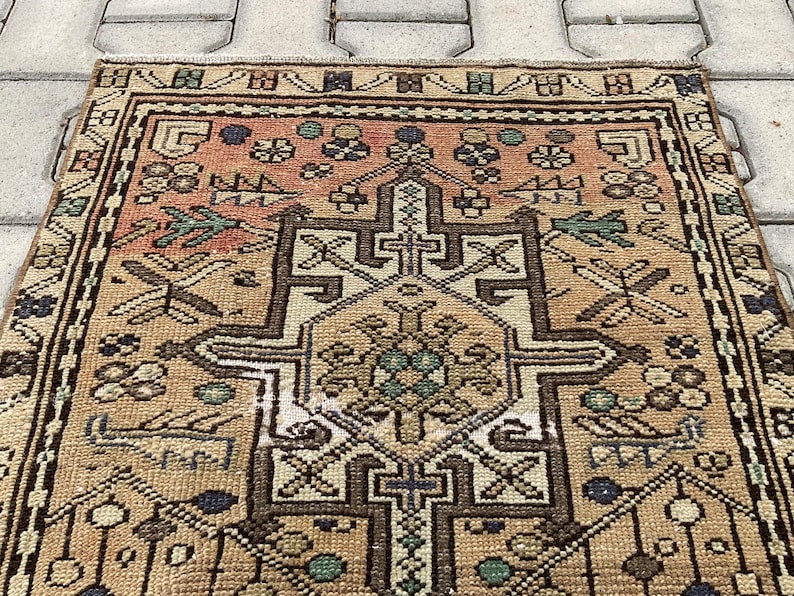 Peut inclure: Un tapis rectangulaire vintage avec un motif g&eacute;om&eacute;trique d&eacute;taill&eacute;. Le tapis pr&eacute;sente un motif de m&eacute;daillon central dans des tons de marron, beige et p&ecirc;che, avec des touches de bleu et de vert. La bordure est marron fonc&eacute;.