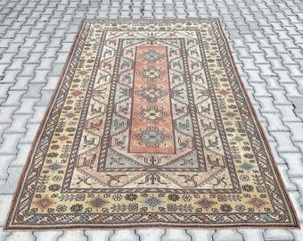 May include: Rectangular, vintage-style rug with an intricate geometric pattern. The rug features a central peach-colored panel surrounded by beige, blue, and brown borders. The design includes floral and geometric motifs, creating a traditional aesthetic.