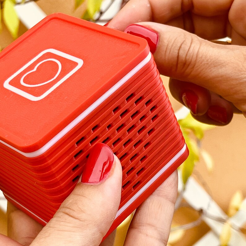 May include: A red and white portable speaker with a heart-shaped icon on the front. The speaker has a grid pattern on the side.