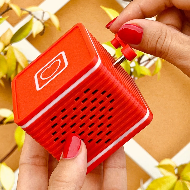 May include: A red and white portable speaker with a heart-shaped logo and a speaker grille. The speaker has a small, white knob on the top.