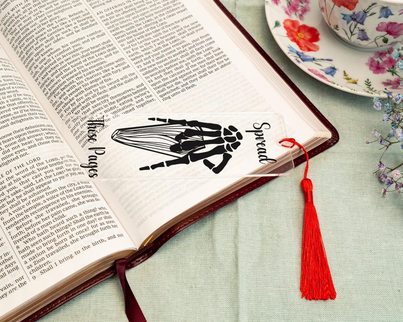 May include: A clear bookmark with a black skeletal hand design and the text "Spread These Pages". The bookmark has a red tassel.