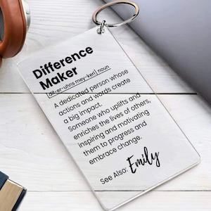 May include: A clear acrylic keychain with the word "Difference Maker" defined as "a dedicated person whose actions and words create a big impact." The keychain also includes the text "See Also: Emily".