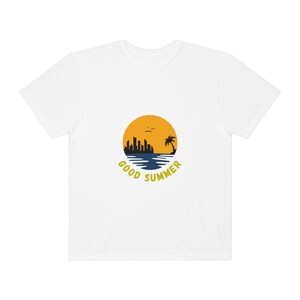 May include: White t-shirt with a graphic of a sunset over a city skyline and palm tree. The text "GOOD SUMMER" is written in a circle around the graphic.