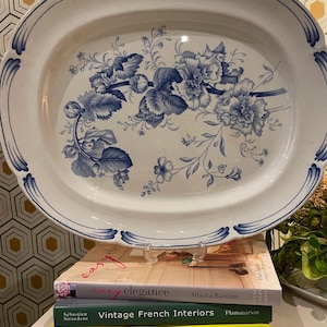 May include: A white oval platter with a blue and white floral design. The platter is sitting on top of three books. The top book is titled "easy elegance" by Atlanta Bartlett. The middle book is titled "Vintage French Interiors" by Flammarion. The bottom book is titled "ZOE SUGG Cordially Invited".