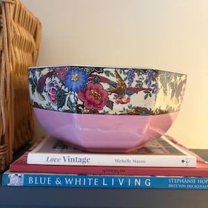 Puede incluir: Un cuenco de cerámica rosa con un diseño floral y de pájaros, apoyado en libros titulados "Love Vintage" y "Blue & White Living". El cuenco tiene una base rosa claro y un borde estampado con flores y pájaros.