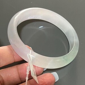 Op de afbeelding: Een doorschijnende jade armband. De armband is lichtgroen en wit van kleur, met een glad, gepolijst oppervlak. De jade is een natuursteen en de armband is een klassiek sieraad. Diameter ongeveer 6,5 cm.