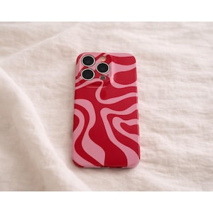 Könnte beinhalten: Rote und rosa Handyhülle mit einem wellenförmigen Muster. Die Hülle hat eine glänzende Oberfläche und drei Kameraausschnitte. Das Design ist eine Mischung aus leuchtendem Rot und Hellrosa und erzeugt eine Retro-Ästhetik.