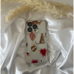 May include: Clear phone case with a colorful design featuring hearts, eyes, and a leopard print. The case has a cutout for the camera lens.