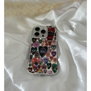 May include: Clear phone case with a colorful heart design. The hearts feature eye motifs and various patterns in shades of red, purple, blue, and green. The case has a clear border and covers the phone's back.