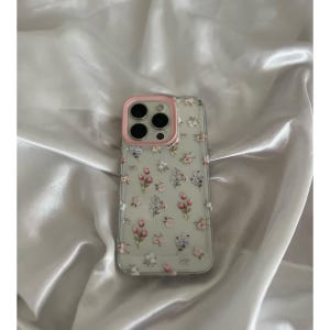 Pode incluir: Capa de telefone transparente com um padr&atilde;o floral com flores rosa, roxas e brancas. A capa tem uma borda rosa ao redor das lentes da c&acirc;mera.