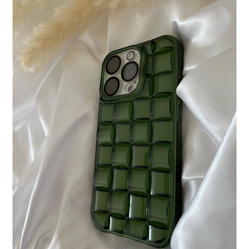 May include: A green phone case with a textured, quilted design. The case has a raised camera bump with three lenses.