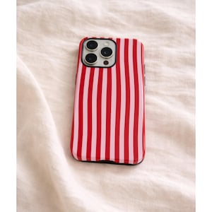 Op de afbeelding: Een rood-roze gestreepte telefoonhoes. De hoes heeft een zwarte rand en bedekt de achterkant en zijkanten van de telefoon. De hoes heeft een verticaal streepjespatroon met afwisselend rode en roze strepen.