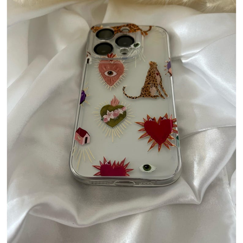 May include: A clear phone case with a colorful design featuring hearts, eyes, and a leopard print. The case has a raised camera bump and a clear back.