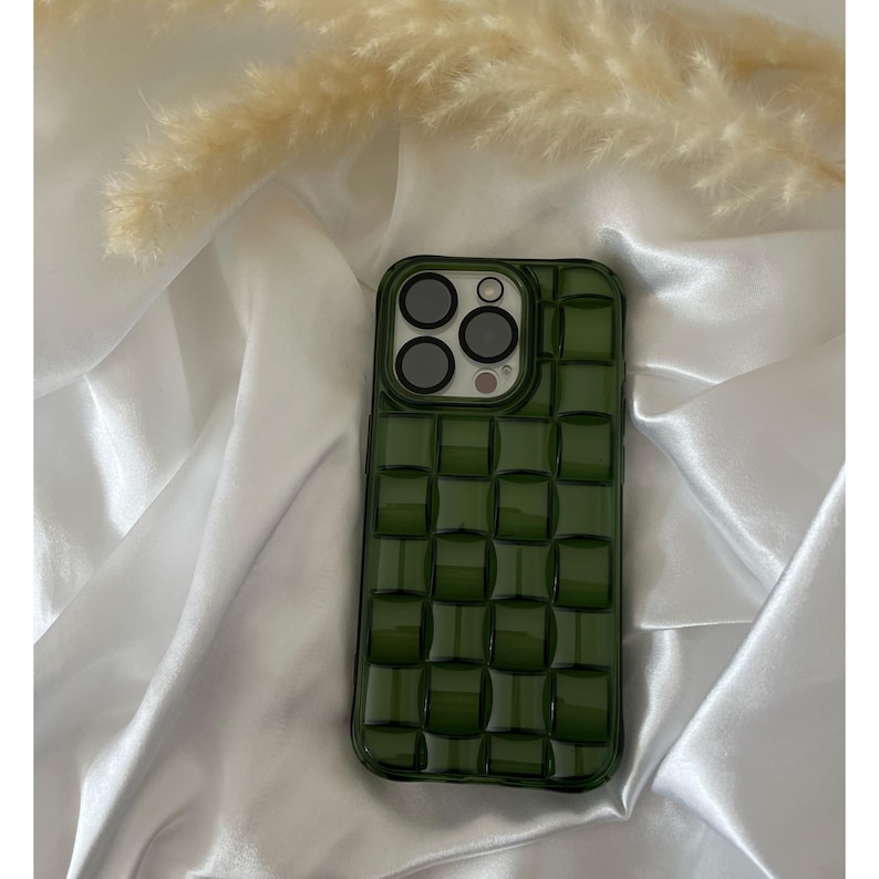 May include: A green phone case with a textured, quilted design. The case has a raised camera bump with three black camera lenses.