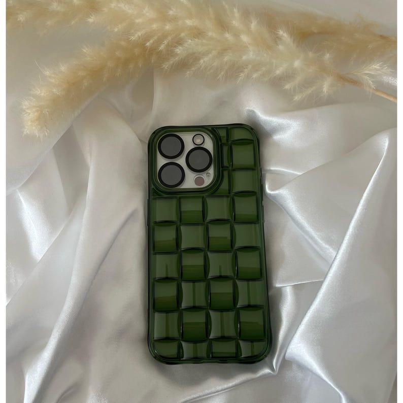 May include: A green phone case with a raised checkered pattern. The case has a camera lens cutout with three black circles.
