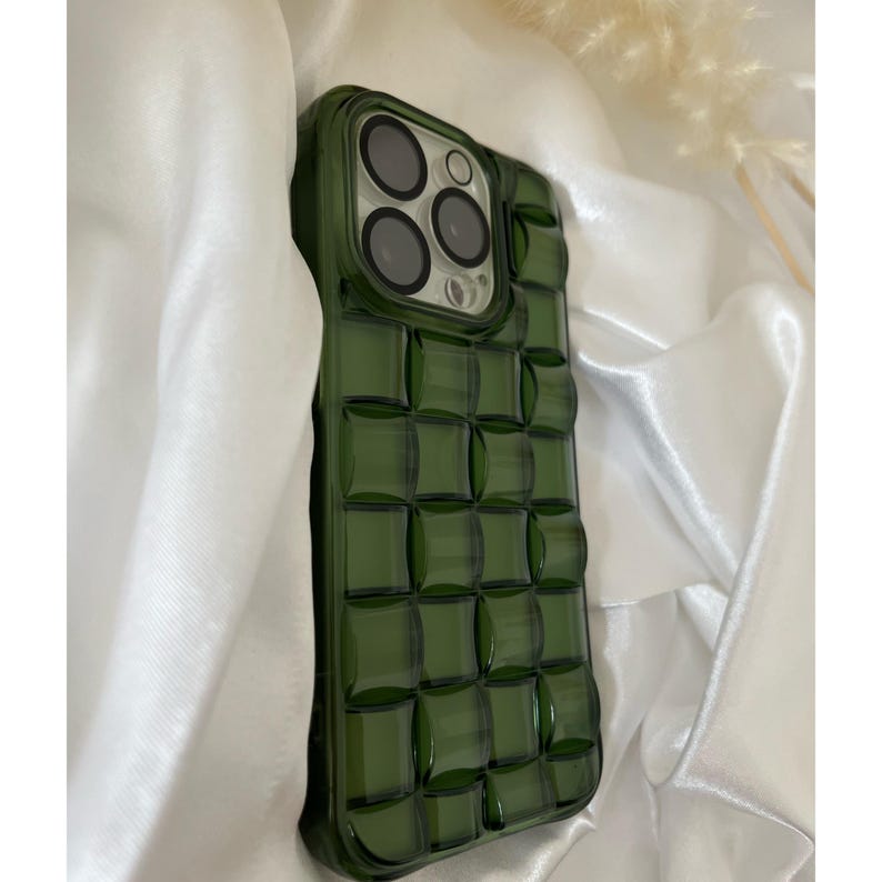 May include: A green phone case with a textured, square pattern. The case has a raised camera bump with three lenses.