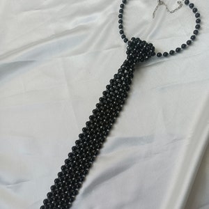 Pu&ograve; includere: Una collana a cravatta con perline nere e chiusura argentata. Le perline sono disposte in un motivo che ricorda una cravatta.