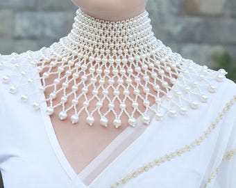 May include: A white pearl choker necklace with a cascading design. The necklace is made of small, round pearls and is strung on a delicate wire. The necklace is a statement piece and would be perfect for a special occasion.