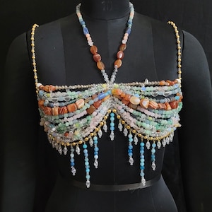 May include: A beaded top in various colors, including orange, green, pink, and blue, is displayed on a black mannequin. The top features multiple strands of beads, with a halter-style neckline and dangling bead accents.
