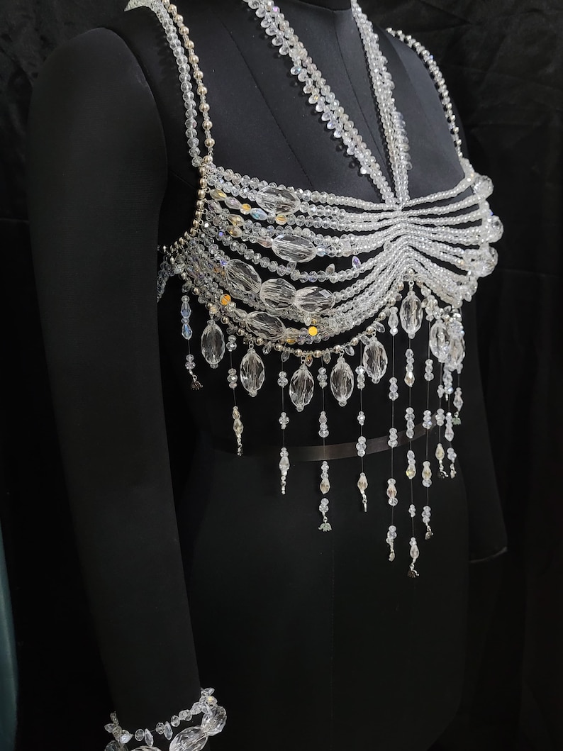 May include: A crystal beaded top with a halter neckline and a fringe design. The top is made of clear crystals and has a silver-toned metal clasp.