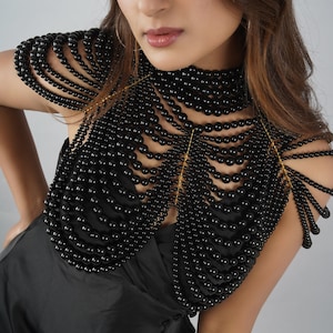 May include: A black beaded choker necklace with a delicate gold chain detail. The necklace is layered and forms a collar around the neck, extending to the shoulders.