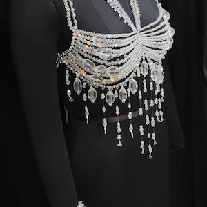 May include: A crystal beaded top with a delicate, layered design. The top features a variety of crystal shapes and sizes, including teardrop, round, and oval beads. The top is accented with small gold beads.