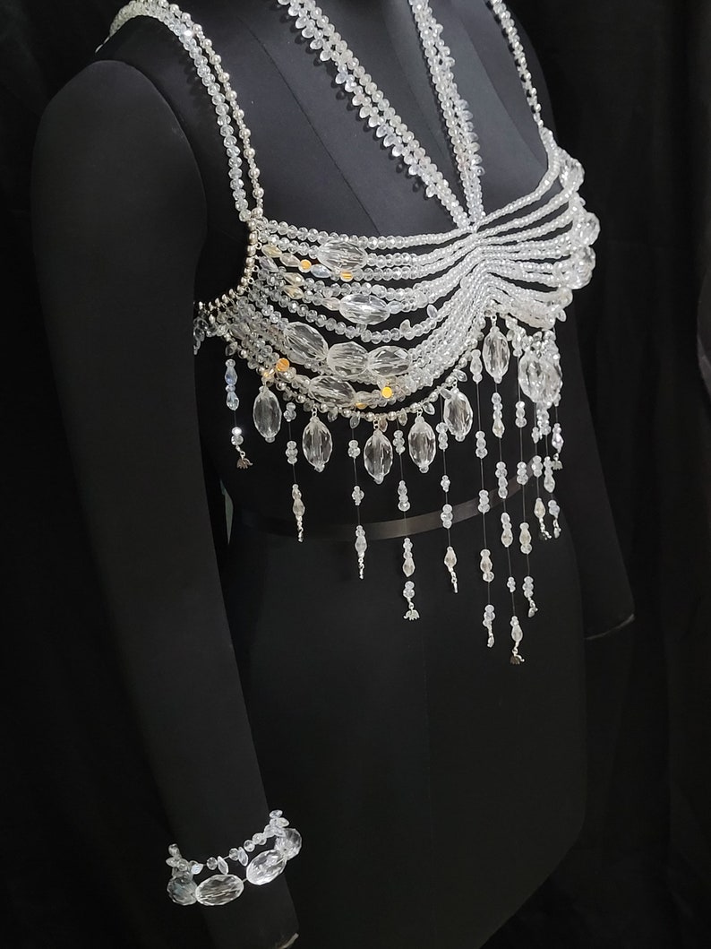 May include: A crystal beaded top with a delicate, layered design. The top features a variety of crystal shapes and sizes, including teardrop, round, and oval beads. The top is accented with small gold beads.