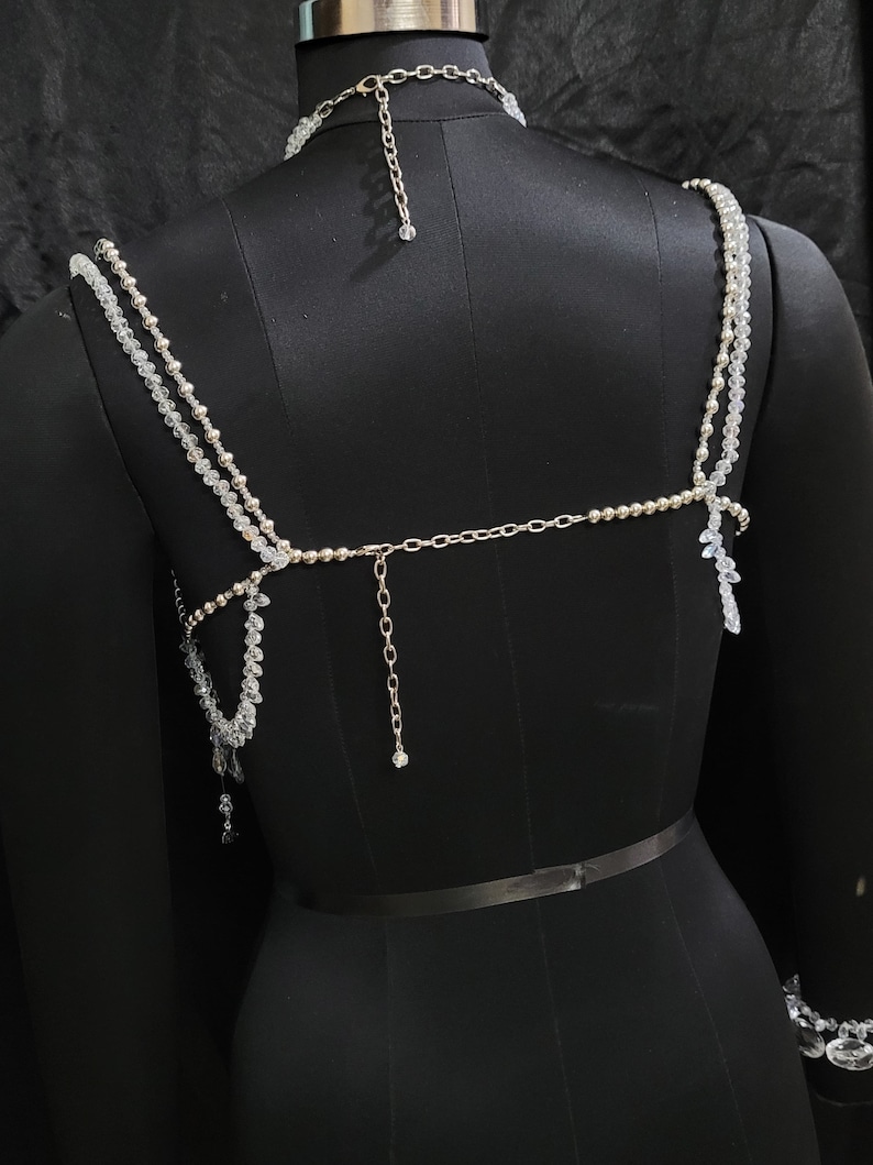 May include: A silver and clear crystal beaded body chain with a matching choker necklace. The chain is made of small, round beads and has a delicate, feminine look.