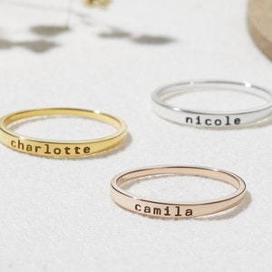 May include: Three thin gold, silver, and rose gold rings with the names "charlotte", "nicole", and "camilla" engraved on them.