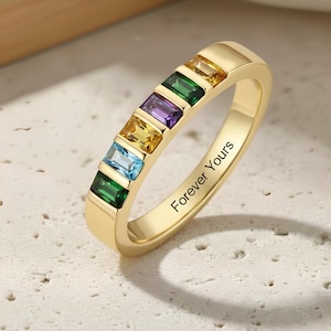 May include: A gold-colored ring with a row of colorful rectangular gemstones. The gemstones are green, blue, yellow, purple, and green. The ring has the inscription "Forever Yours".