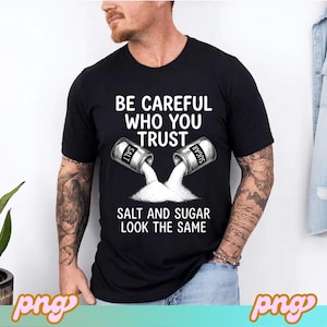 以下が含まれることがあります： 「BE CAREFUL WHO YOU TRUST」の文字が入った黒いTシャツ。塩と砂糖の容器から中身が注がれるデザインで、下に「SALT AND SUGAR LOOK THE SAME」の文字。カジュアルウェアです。