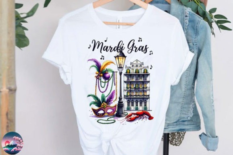 May include: White t-shirt with a colorful Mardi Gras design featuring a mask, beads, a street lamp, a building, and a crawfish. The text "Mardi Gras" is written in black cursive.