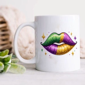 May include: White ceramic mug with a green, gold, and purple glitter lips design. The lips are outlined in gold and have a sparkle effect.